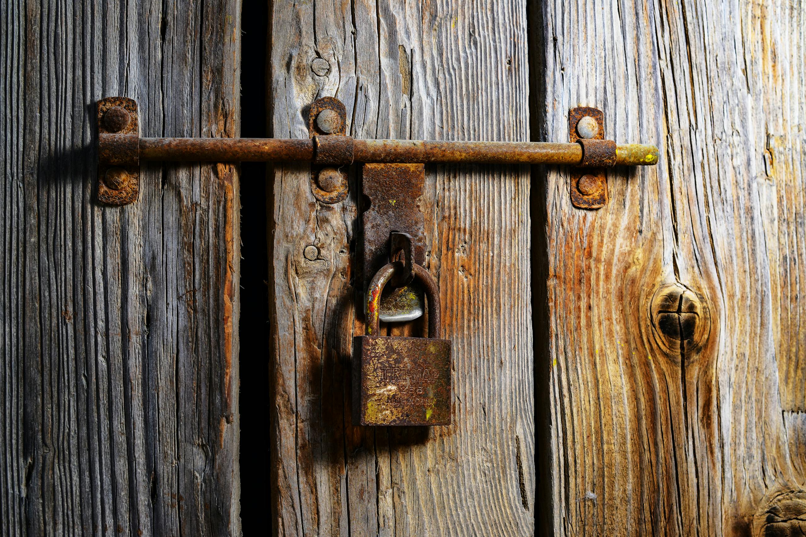 Close-up of a rusty padlock securing a vintage wooden door, highlighting texture and decay.